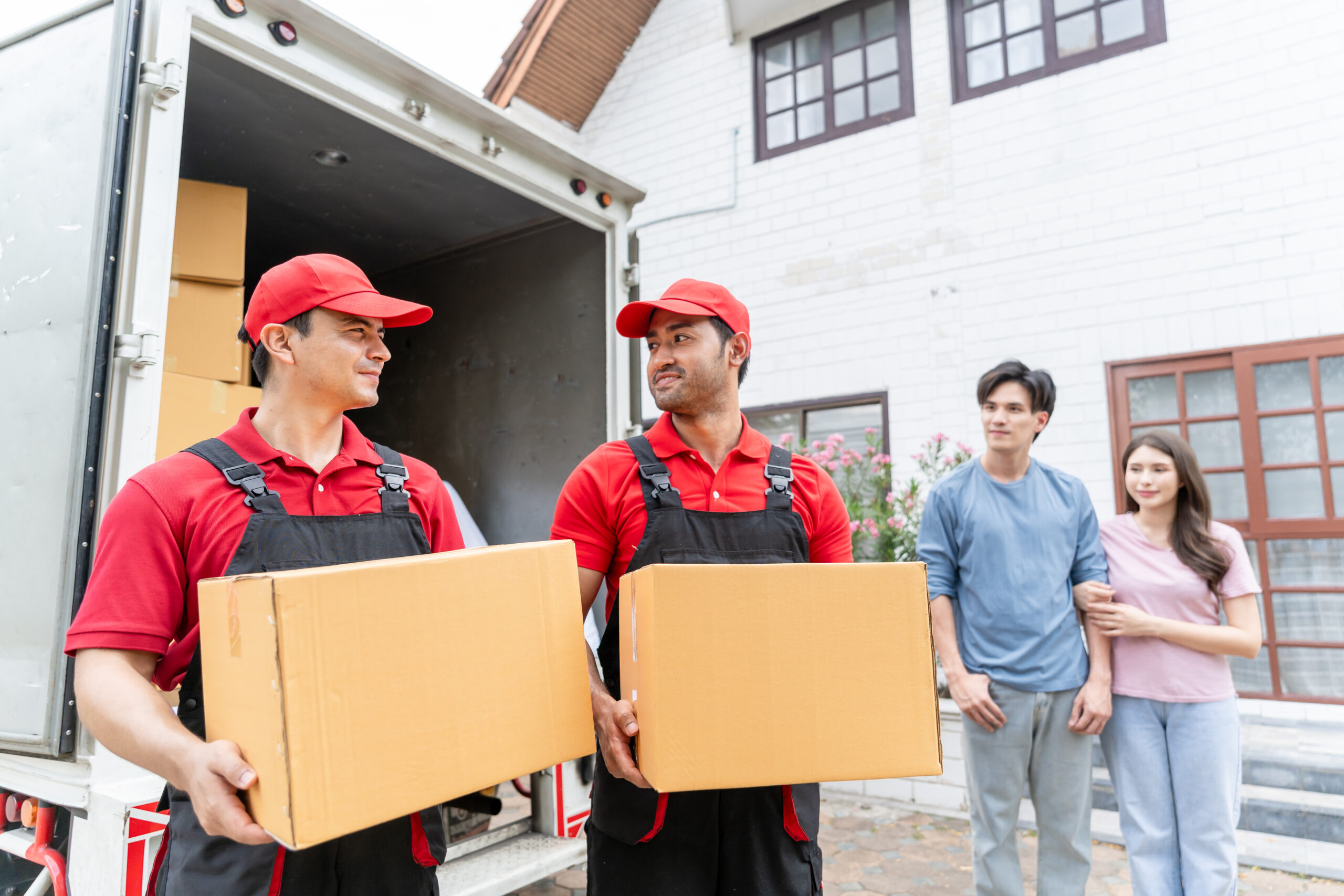 Caucasian delivery man worker delivering package to young couple in house. Attractive courier employee working and deliver box cardboard from car truck infront of new house of new marriage partner.